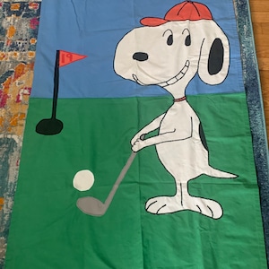 May include: A white and black cartoon dog wearing a red hat and holding a golf club. The dog is on a green golf course with a golf flag and a white golf ball.