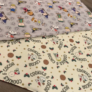 May include: Two fabric squares with a repeating pattern. The top square is gray with a white pattern of cartoon characters. The bottom square is cream with a brown, green, and gold pattern of cartoon characters and the text "Cookies & Cocoa".