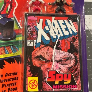May include: X-Men Spy Mission action figure set featuring comic book cover art. Includes two small action figures and a comic book cover. The packaging is red, orange, and purple with the Toy Biz logo.