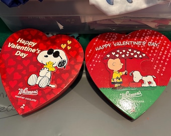 May include: Two heart-shaped Whitman's chocolate boxes with Snoopy and Woodstock, and Charlie Brown and Snoopy illustrations. The boxes are red with white text that reads "Happy Valentine's Day".