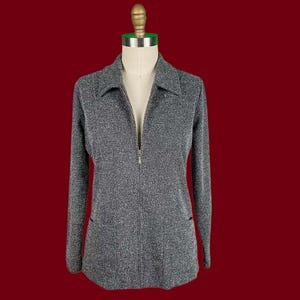 May include: A grey zip-up jacket with long sleeves and a collared neckline. The jacket has a textured, speckled appearance and two front pockets. The zipper is silver-toned, and the jacket is displayed on a mannequin against a red background.