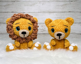 May include: Two crocheted stuffed animals, a lion and a bear, sitting on a white fluffy surface. The lion has a brown mane and blue eyes. The bear has brown fur and blue eyes. Both animals have white crocheted paws.