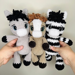 May include: Three crocheted stuffed animals: a gray donkey, a brown horse, and a black and white zebra. Each animal has a white face with black eyes and a black nose.