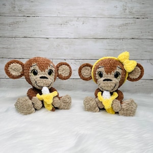 May include: Two crocheted monkey toys sitting on a white fluffy surface. Both monkeys are brown with yellow accents and are holding a yellow banana. One monkey has a yellow bow on its head.