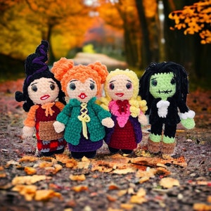 K&ouml;nnte beinhalten: Vier geh&auml;kelte Puppen, die als Hexen verkleidet sind. Die Puppen stehen auf einem Bett aus Herbstlaub. Die Puppen tragen verschiedene farbige Kleider und H&uuml;te.
