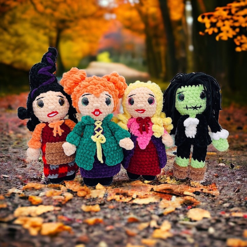 K&ouml;nnte beinhalten: Vier geh&auml;kelte Puppen, die als Hexen verkleidet sind. Die Puppen stehen auf einem Bett aus Herbstlaub. Die Puppen tragen verschiedene farbige Kleider und H&uuml;te.