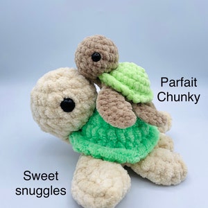 May include: Two crocheted plush turtle toys, one larger than the other, with green shells and brown bodies. The smaller turtle is riding on the back of the larger turtle. The larger turtle has the text "Sweet snuggles" written below it. The smaller turtle has the text "Parfait Chunky" written above it.