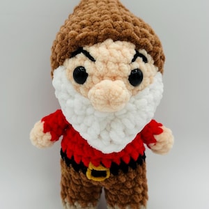 May include: A handmade crochet dwarf doll with a brown hat, face, and legs. The doll has a white beard, red shirt, and black belt with a gold buckle. The eyes are large and black.