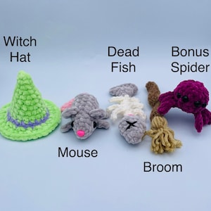 May include: A set of crocheted Halloween decorations, including a green witch's hat, a grey mouse, a grey dead fish, a brown and beige broom, and a purple spider.