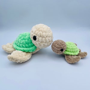 May include: Two crocheted sea turtle toys. The larger turtle is cream colored with a green shell. The smaller turtle is brown with a green shell.