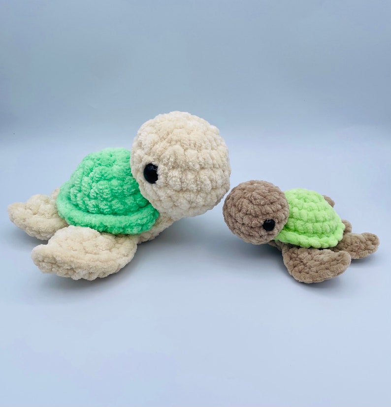 May include: Two crocheted sea turtle toys. The larger turtle is cream colored with a green shell. The smaller turtle is brown with a green shell.