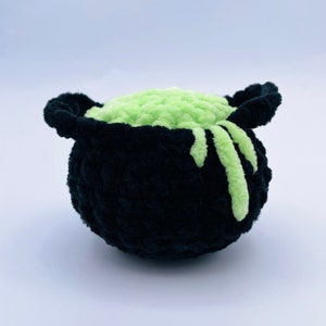 May include: A black crocheted cauldron filled with green slime. The slime is dripping down the sides of the cauldron.