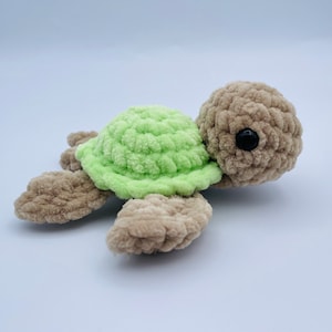 May include: A crocheted green and brown turtle toy. The turtle has a green shell and brown legs and head. The turtle has black eyes.