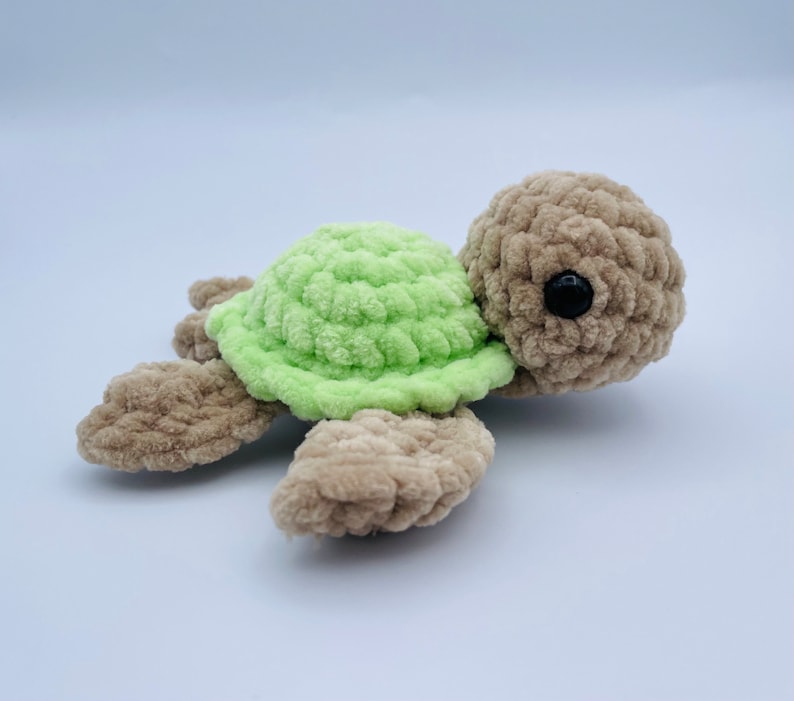 May include: A crocheted green and brown turtle toy. The turtle has a green shell and brown legs and head. The turtle has black eyes.