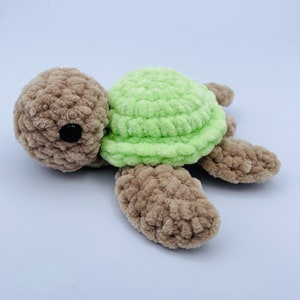 May include: A crocheted stuffed turtle toy with a brown body and green shell. The turtle has black eyes and a simple, friendly expression.