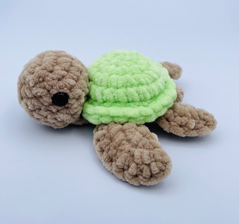 May include: A crocheted stuffed turtle toy with a brown body and green shell. The turtle has black eyes and a simple, friendly expression.