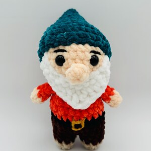 May include: A handmade crochet gnome doll with a teal hat, white beard, and a red and brown outfit. The gnome has large black eyes and a tan nose. The doll is a whimsical decorative item.