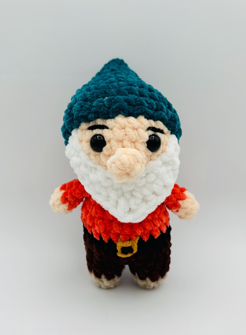 May include: A handmade crochet gnome doll with a teal hat, white beard, and a red and brown outfit. The gnome has large black eyes and a tan nose. The doll is a whimsical decorative item.