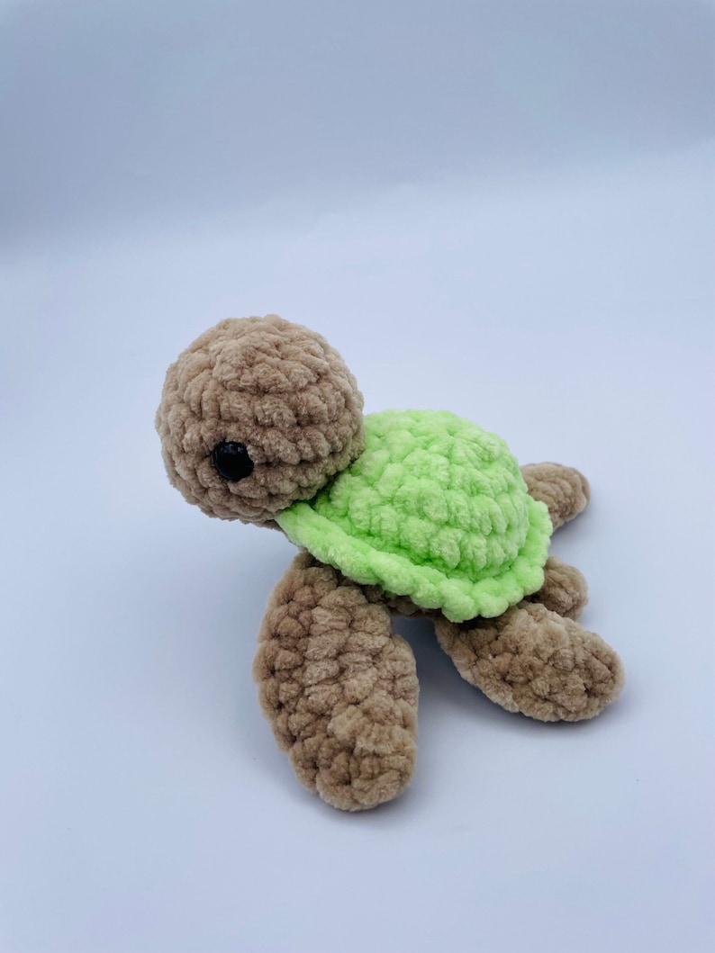 May include: A crocheted turtle toy with a brown body and green shell. The turtle has black eyes and a small, round head.
