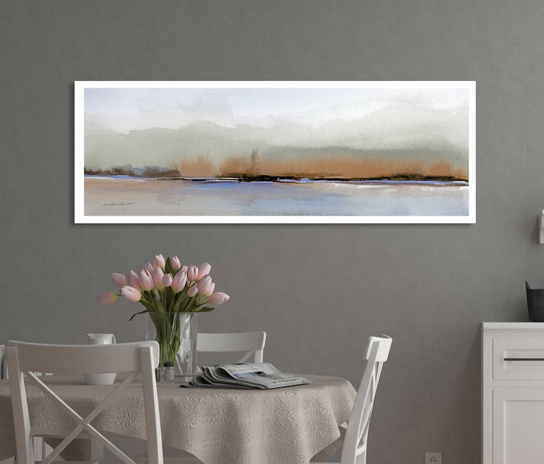 Puede incluir: Una pintura abstracta horizontal larga con un marco blanco. La pintura presenta un esquema de color azul claro, gris y marr&oacute;n con una l&iacute;nea horizontal sutil que representa un horizonte. La pintura est&aacute; colgada en una pared gris sobre una mesa blanca con un mantel blanco y un jarr&oacute;n de tulipanes rosas.