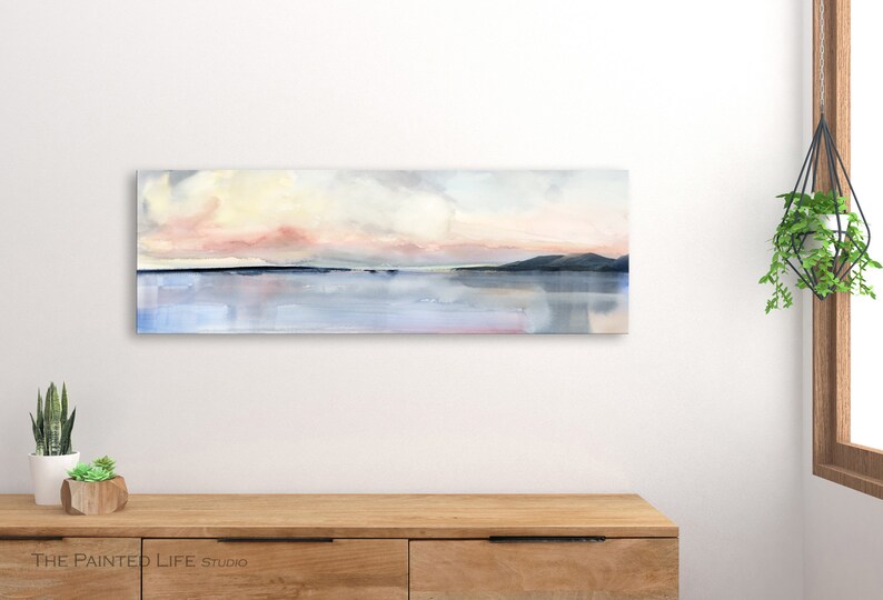 May include: A watercolor painting of a landscape with a pink and yellow sky, a dark blue line representing water, and a dark blue mountain range in the distance.