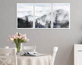 May include: A set of three framed watercolor paintings depicting a misty mountain landscape with a forest of trees. The paintings are in shades of gray and blue, with a hint of green in the trees.