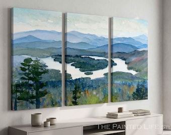 May include: A three-panel watercolor canvas print depicting a landscape with a winding river, dense green forests, and layered blue mountains under a pale sky. The artwork features visible brushstrokes and a serene, natural color palette.