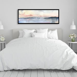 May include: A white bed with a white duvet cover and white pillows in a bedroom with a framed abstract watercolor painting of a pink and blue sunset over a body of water. The painting is hanging on a white wall above the bed.