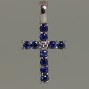 May include: A silver cross pendant with blue sapphires and a single diamond in the center.