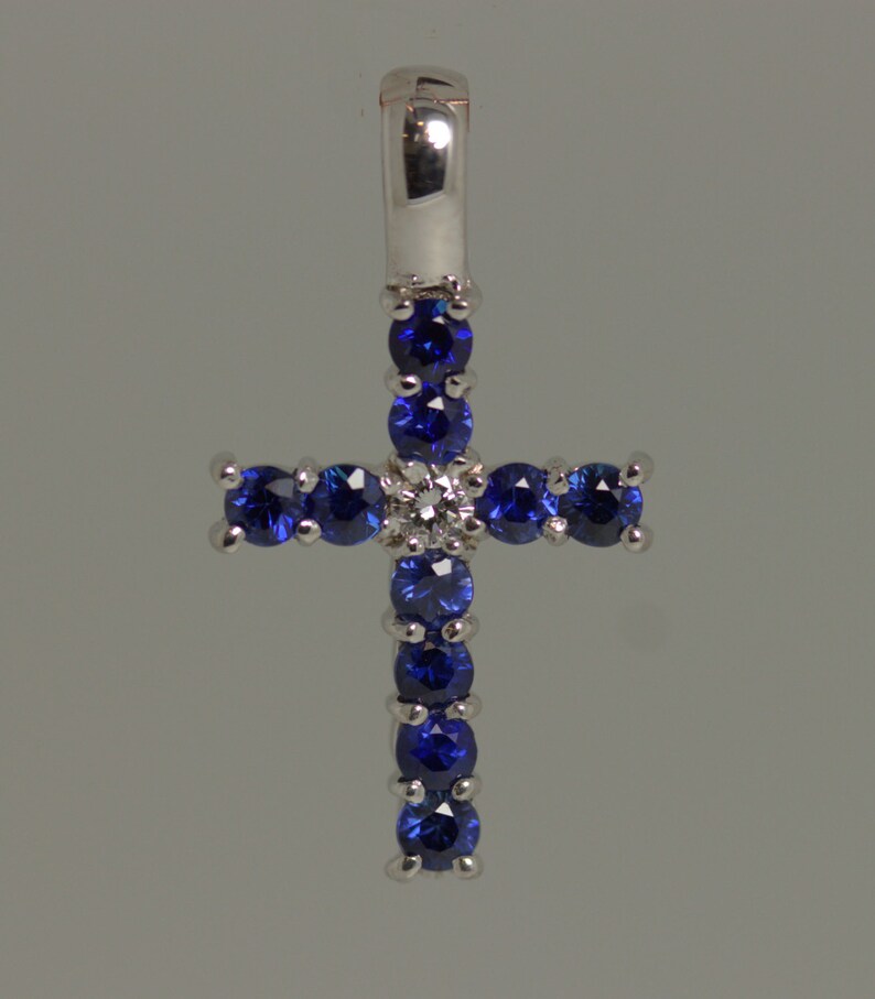 May include: A silver cross pendant with blue sapphires and a single diamond in the center.