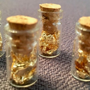 May include: Five small glass bottles with cork stoppers, each filled with gold leaf flakes.