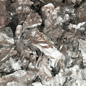 May include: A close-up of a pile of shiny, metallic silver flakes. The flakes are irregularly shaped and have a slightly textured surface.