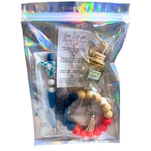 Könnte beinhalten: Eine transparente Plastiktüte gefüllt mit Autodiffusor-Artikeln. Die Artikel umfassen einen Autodiffusor mit blau-weißem Muster, einen Schlüsselanhänger aus Holzperlen mit roten, blauen und weißen Perlen, eine kleine Flasche "Christmas Wreath" Duftöl und eine weiße Karte mit Anweisungen zur Verwendung des Autodiffusors.