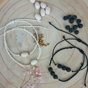 Könnte beinhalten: Handgefertigte Armbänder mit Natursteinperlen und goldenen Akzenten. Das Bild zeigt weiße und schwarze Kordelarmbänder mit ovalen und runden Perlen. Zusätzliche Perlen und Materialien sind auf einer Holzoberfläche verstreut.