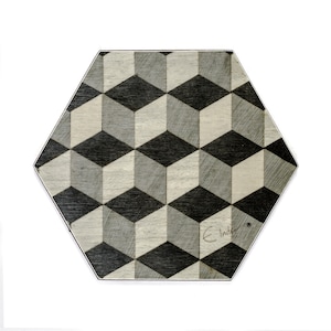 Op de afbeelding: Een zeshoekig houten bord met een zwart-wit geometrisch patroon van kubussen. Het bord is onderaan rechts gesigneerd met "E. Inder".