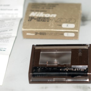 Op de afbeelding: Een bruin plastic camera-scherpstelscherm met een heldere glazen inzet. Het scherm is gelabeld "Nikon IF-501/N200 TYPE E".