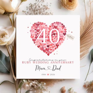 May include: A white card with a heart composed of red hearts, featuring the number 40 in white. The text reads "Congratulations on your Ruby Wedding Anniversary Mum & Dad 1986 2026" with a small tag that says "With love".