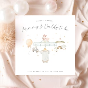 May include: Congratulations Mummy & Daddy to be card with a watercolour illustration of a baby's nursery with a shelf, a bunny, a mobile, a balloon, booties, and a onesie. The text reads "Baby Richardson due October 2025".