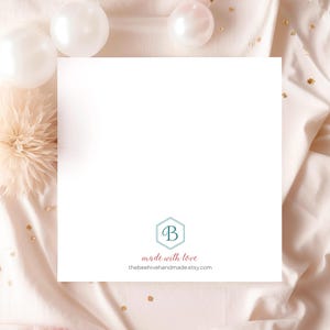 Op de afbeelding: Een witte kaart met een lichtblauwe zeshoek met de letter "B" erin. De tekst "made with love" staat onder de zeshoek, en de tekst "thebeehivehandmade.etsy.com" staat daaronder. De kaart ligt op een lichtroze oppervlak met witte en gouden confetti.