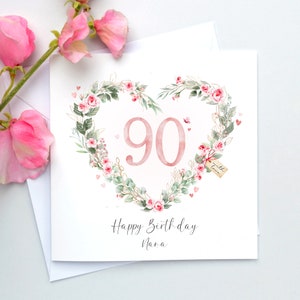 May include: A white card with a pink floral heart design. The number 90 is in the center of the heart. The text "Happy Birthday Nana" is below the heart.
