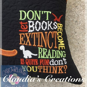 May include: Black pillow with colourful embroidered text that reads "Don't let books become extinct. Reading is quite fun! Don't you think?"  The pillow has a dinosaur design and the text "Claudia's Creations" is embroidered in the bottom right corner.