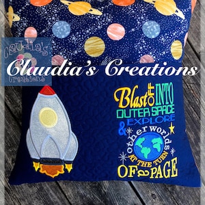 May include: A blue pillow with a rocket ship and the text "Blast into Outer Space & Explore Other Worlds at the Turn of Page". The pillow has a quilted pattern and is decorated with stars and planets.