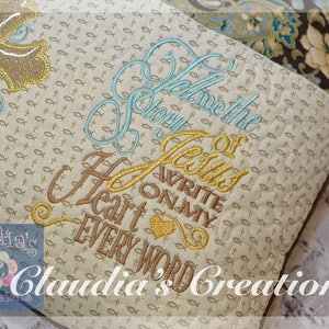 May include: A beige pillow with a gold and blue embroidered cross and the text "Tell me the story of Jesus write on my heart every word". The pillow has a brown and blue floral fabric on the back.