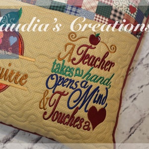 Puede incluir: Una almohada beige con una manzana roja y el texto "A Teacher takes a hand, Opens a Mind & Touches a" bordado en ella. La almohada tiene un diseño de patchwork en la parte posterior.