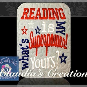 May include: White fabric with red, white and blue embroidery that reads "Reading is my superpower! What's yours?" with a star at the end. The text is in a decorative font. The fabric is quilted and has a subtle texture. The image is from Claudia's Creations.