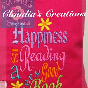 May include: Pink pillow with the text "Happiness is Reading a Very Good Book" embroidered in colourful thread. The pillow has a pocket with the text "Claudia's Creations" embroidered on it.