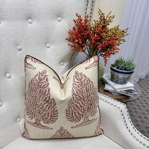 May include: A cream-colored throw pillow with a red tree design. The pillow is sitting on a white chair with a tufted back.