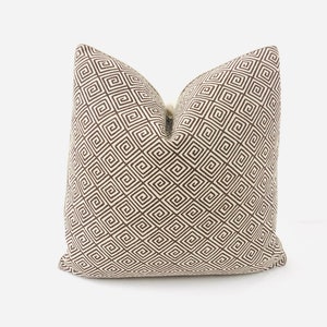 May include: A cream-colored pillow with a brown geometric pattern. The pattern is a repeating design of squares and spirals.