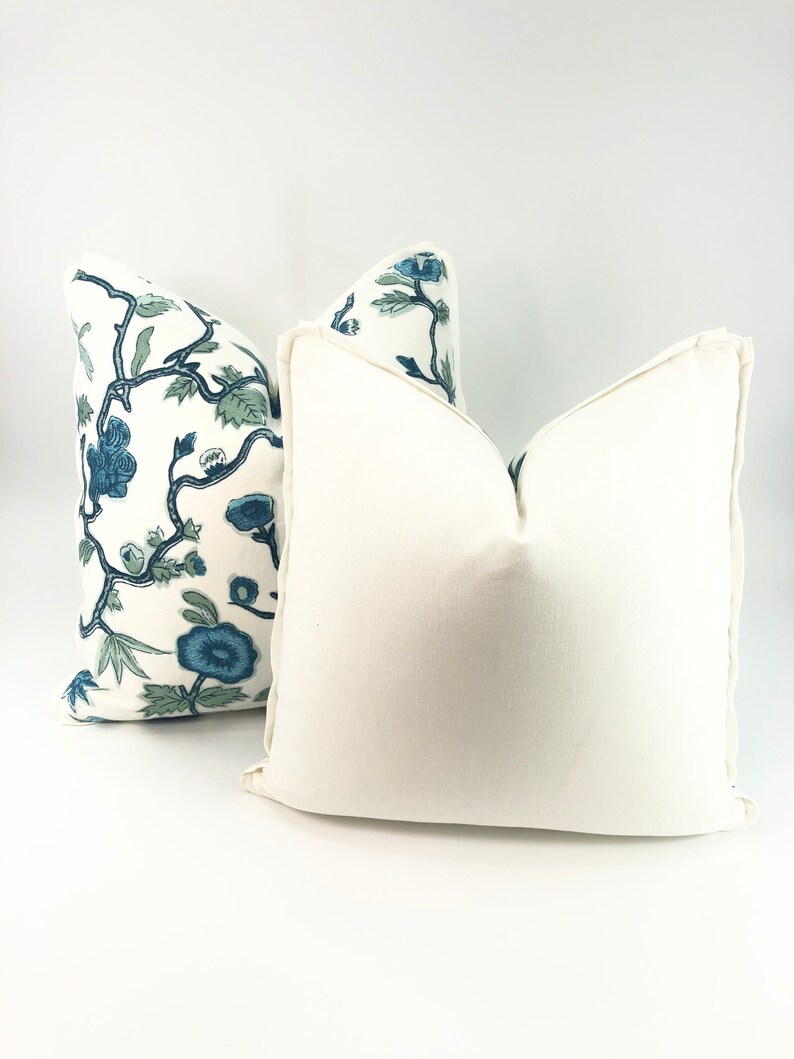 May include: Two decorative throw pillows, one with a white background and a blue and green floral pattern, and the other a solid white pillow.