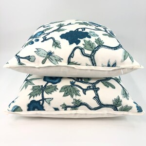 May include: Two white throw pillows with a blue and green floral pattern. The pillows are stacked on top of each other.